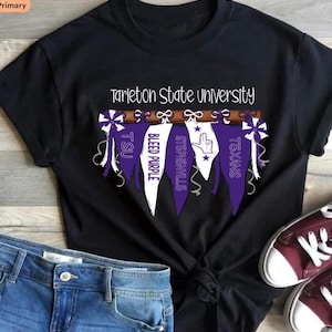 May include: A black short-sleeved t-shirt featuring the text Tarleton State University above a graphic of five hanging pennants in purple and white. The pennants display the text TSU, BLEED PURPLE, STEPHENVILLE, and TEXANS with a hand sign icon.
