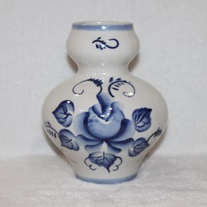 May include: A white ceramic vase with a blue and white floral design. The vase has a round body and a narrow neck.