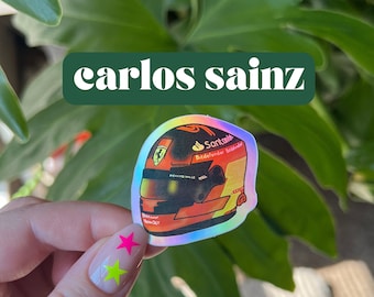 May include: A holographic sticker of a Formula 1 driver's helmet. The helmet is red, black, and yellow with the driver's name "Sainz" and sponsor logos. The sticker is on a white background.