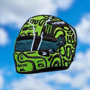 Könnte beinhalten: Gestickter Aufnäher in Form eines Rennhelms. Der Helm ist überwiegend grün mit schwarzen und weißen Akzenten. Das Design enthält das Wort "Android". Der Hintergrund ist ein blauer Himmel mit Wolken.