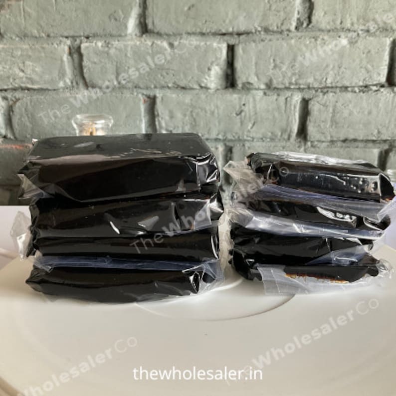 May include: A stack of five black rectangular blocks wrapped in clear plastic, and a stack of six black rectangular blocks wrapped in clear plastic. The blocks are on a white surface.