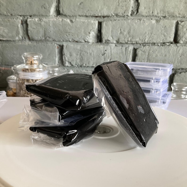 May include: Four black rectangular blocks wrapped in clear plastic, stacked on a white surface. The blocks are smooth and shiny.