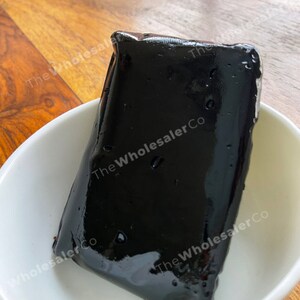 May include: A black, rectangular block of agar agar, a gelatinous substance used in cooking and baking, sits on a white plate. The agar agar is shiny and smooth.