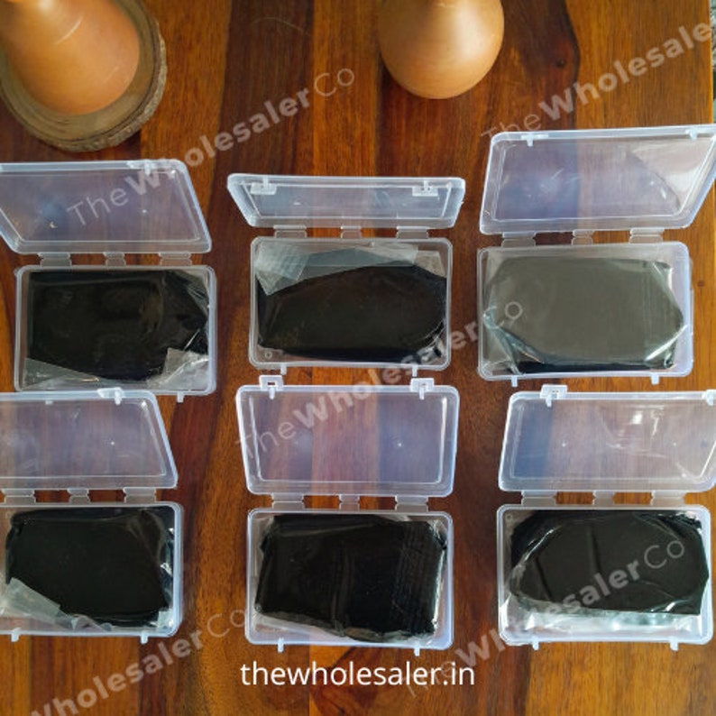 May include: Six clear plastic containers with lids, each containing a black, rectangular block of material. The containers are arranged in two rows of three, on a wooden surface. The text "The Wholesaler Co" is visible on the containers.