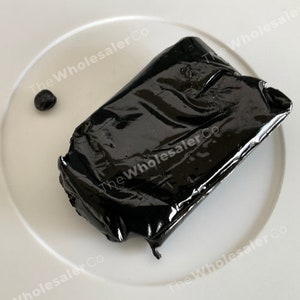 May include: A black, shiny, rectangular block of resin on a white plate. The resin is smooth and has a glossy finish.