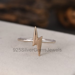 May include: A silver ring with a gold lightning bolt design. The ring is simple and modern.