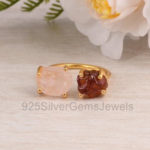 May include: Gold ring with two stones, one pink and one red. The stones are set in a gold band.