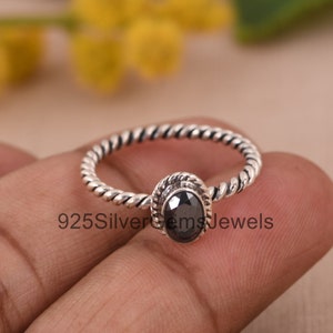 Puede incluir: Un anillo de plata con una piedra ovalada negra engastada en una banda retorcida. El anillo está en un dedo.