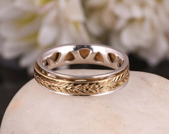 Op de afbeelding: Een zilveren en gouden ring met een decoratief ontwerp van bladeren en een getextureerde rand.