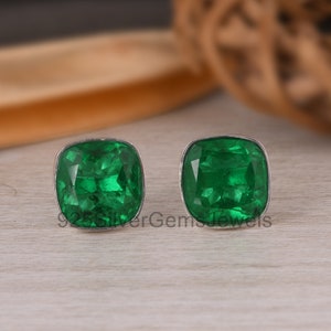 May include: A pair of silver earrings featuring square-shaped green gemstones. The earrings are set in a simple silver setting.