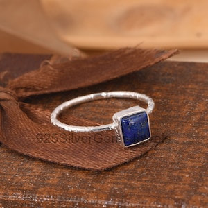 Op de afbeelding: Een zilveren ring met een vierkante blauwe lapis lazuli edelsteen. De ringband heeft een getextureerde afwerking.