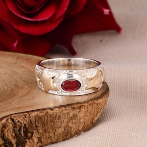May include: A silver ring with a red gemstone and two gold stars on each side.