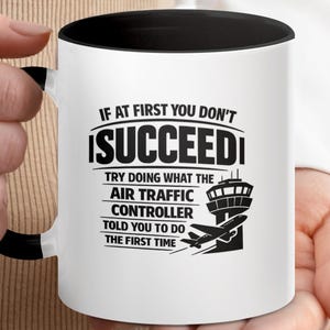 May include: White ceramic mug with a black interior and handle. The mug features the text "IF AT FIRST YOU DON'T SUCCEED, TRY DOING WHAT THE AIR TRAFFIC CONTROLLER TOLD YOU TO DO THE FIRST TIME" in black, with an airplane and control tower graphic.