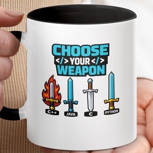 May include: A white ceramic mug with a black interior and handle, featuring the text "CHOOSE YOUR WEAPON" in blue. Below the text are four sword illustrations labelled "C++" with flames, "JAVA" with a blue blade, "C" with a silver hilt, and "PYTHON".