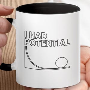May include: White ceramic mug with a black interior and handle. The mug features the text "I HAD POTENTIAL" in black block letters, along with a black and white graphic of a ball rolling down a ramp. The mug is held by a person.