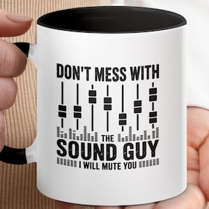 Może przedstawiać: Biały ceramiczny kubek z czarnym wnętrzem i uchwytem. Kubek zawiera czarny napis "DON'T MESS WITH THE SOUND GUY I WILL MUTE YOU" wraz z grafiką suwaków miksowania dźwięku.
