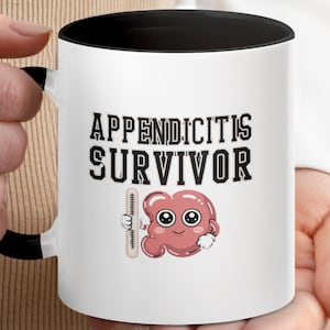 May include: White ceramic mug with a black interior and handle. The mug features the text "APPENDICITIS SURVIVOR" in bold, black letters. Below the text is a cartoon illustration of an appendix holding a thermometer. The mug is held by a person.