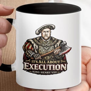 May include: White ceramic mug with a black interior and handle, featuring a graphic of King Henry VIII holding an axe. The text "IT'S ALL ABOUT EXECUTION" and "KING HENRY VIII" are displayed below the image. The mug is held by a person.