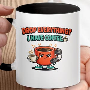May include: White ceramic coffee mug with a black interior and handle. The mug features a cartoon coffee cup character holding a small cup and a telephone, with the text "DROP EVERYTHING? I HAVE COFFEE."