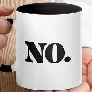 May include: White ceramic mug with a black interior and handle. The word "NO." is printed in large, bold, black letters on the front of the mug. The mug is held by a person.