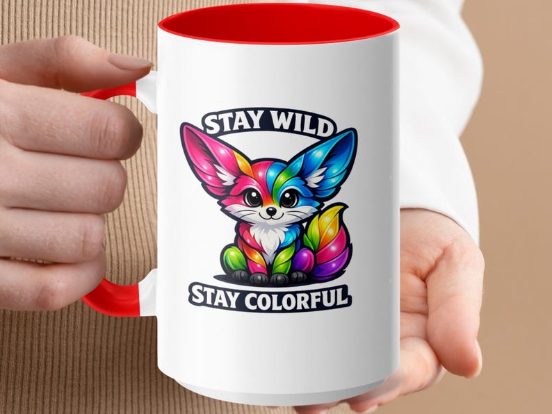 White mug with red rim featuring a colorful cartoon fox and text "STAY WILD STAY COLORFUL".