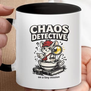 Op de afbeelding: Witte keramische mok met een zwarte binnenkant en handvat. De mok heeft een cartoon illustratie van een muis detective met een vergrootglas, met de tekst "CHAOS DETECTIVE" en "on a tiny mission".