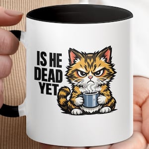 May include: White ceramic mug with a black interior and handle. The mug features a cartoon illustration of an angry cat holding a coffee cup, with the text "IS HE DEAD YET" in black. The cat is brown, orange, and white.