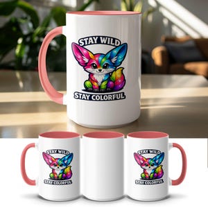 White mug with pink handle featuring a rainbow fox illustration and "STAY WILD STAY COLORFUL" text.