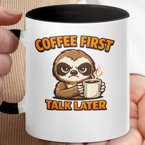 May include: White coffee mug with a black interior and handle. The mug features a cartoon sloth holding a coffee cup, with the text "COFFEE FIRST TALK LATER" in orange and brown.