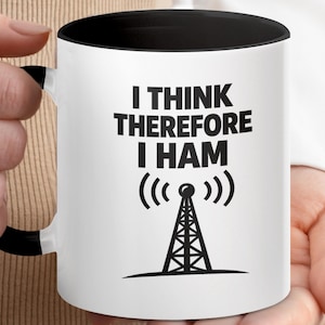 Peut inclure: Un mug en céramique blanche avec un intérieur et une anse noirs. L'extérieur présente le texte noir I THINK THEREFORE I HAM au-dessus d'un graphique noir représentant une tour de transmission radio avec des ondes de signal émanant du sommet.