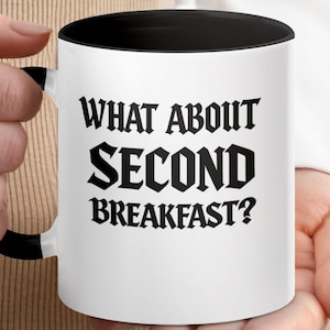 Peut inclure: Mug en céramique blanche avec intérieur et anse noirs. Le mug affiche le texte "WHAT ABOUT SECOND BREAKFAST?" en lettres noires et grasses. Un cadeau amusant sur le thème de la nourriture.
