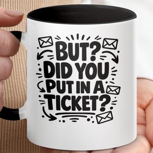 May include: White ceramic mug with a black interior and handle. The mug features the text "BUT? DID YOU PUT IN A TICKET?" in black, along with envelope graphics and arrows. The mug is held by a person.