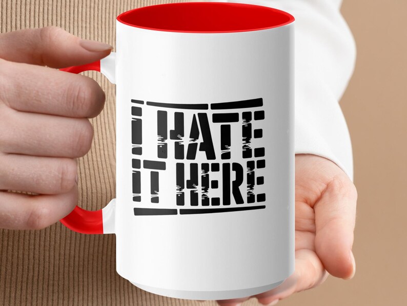 White mug with red handle and "I HATE IT HERE" text.