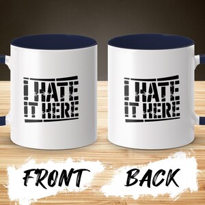 Two white mugs with navy blue handles, displaying "I HATE IT HERE" text.