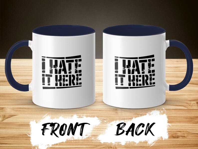Two white mugs with navy blue handles, displaying "I HATE IT HERE" text.