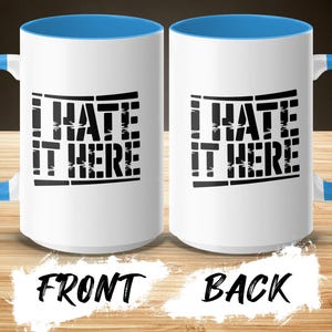 White mugs with blue handles, showing "I HATE IT HERE" text on front and back.