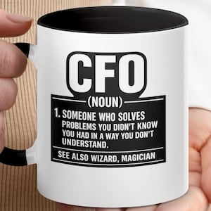 May include: White ceramic mug with a black interior and handle, featuring the bold text "CFO (NOUN)". The mug's design includes a definition: "SOMEONE WHO SOLVES PROBLEMS YOU DIDN'T KNOW YOU HAD IN A WAY YOU DON'T UNDERSTAND."