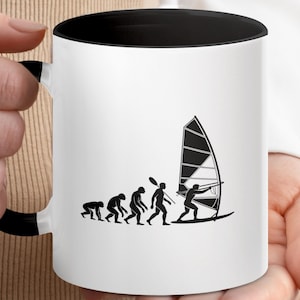 May include: White ceramic mug with a black interior and handle. The mug features a black graphic depicting the evolution of windsurfing, from ape-like figures to a person windsurfing on a board with a sail. The mug is held by a person.