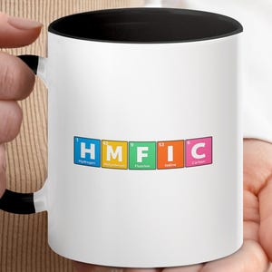 Può includere: Tazza in ceramica bianca con interno e manico neri. La tazza presenta le lettere "HMFIC" in un design colorato della tavola periodica. Le lettere rappresentano Idrogeno, Molibdeno, Fluoro, Iodio e Carbonio.