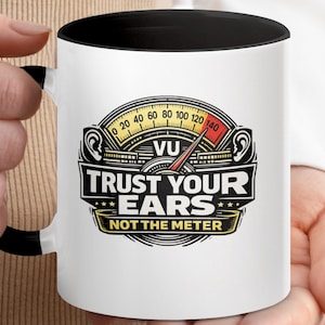 Peut inclure: Mug en céramique blanche avec intérieur et anse noirs. Il présente un graphisme avec un design de voltmètre et le texte "TRUST YOUR EARS NOT THE METER". Le design comprend des illustrations d'oreilles et un code couleur jaune, rouge et noir.