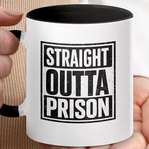 Puede incluir: Taza de cerámica blanca con interior y asa negros. La taza presenta el texto "STRAIGHT OUTTA PRISON" en un diseño rectangular negro desgastado.