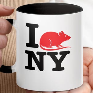 May include: White ceramic mug with a black handle and interior. The mug features the text "I NY" in black block letters, with a red rat graphic replacing the "O". A fun, novelty item.