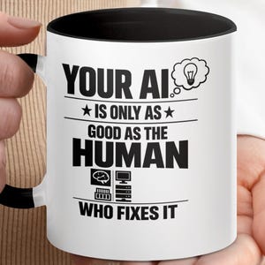 May include: White ceramic mug with a black interior and handle. The mug features the text "YOUR AI IS ONLY AS GOOD AS THE HUMAN WHO FIXES IT" in bold black letters. A lightbulb icon is on the right side of the text.