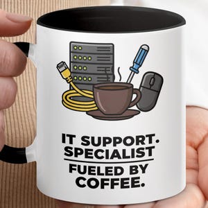 May include: White coffee mug with a black interior and handle. The mug features illustrations of IT equipment and a coffee cup. Text on the mug reads: IT SUPPORT. SPECIALIST. FUELED BY COFFEE.