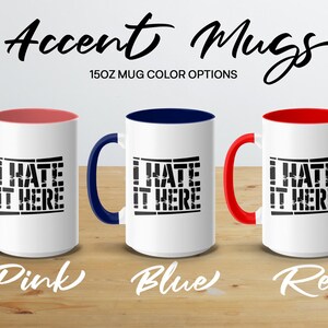 Three white mugs with "I HATE IT HERE" in black, in pink, blue, and red options.