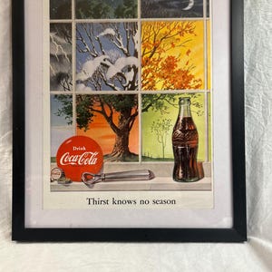 May include: Framed vintage Coca-Cola advertisement. The artwork depicts a window divided into seasonal scenes. A bottle of Coca-Cola sits in front of the window. The text "Drink Coca-Cola" is visible, along with the phrase "Thirst knows no season."