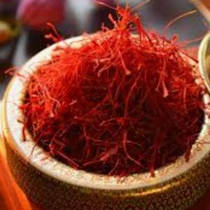 May include: A close-up of a bowl filled with vibrant red saffron threads. The bowl has a decorative rim and sits on a blurred background. The saffron threads are the focal point, showcasing their rich color and texture.
