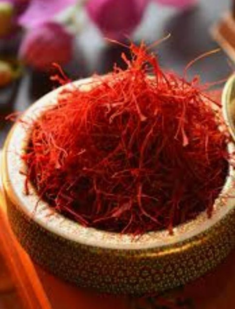 May include: A close-up of a bowl filled with vibrant red saffron threads. The bowl has a decorative rim and sits on a blurred background. The saffron threads are the focal point, showcasing their rich color and texture.