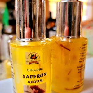 May include: Two bottles of organic saffron serum with silver caps. The yellow liquid contains saffron threads. The label reads "Organic Saffron Serum" and "Net Wght 1.0 fl oz / 30 ml".