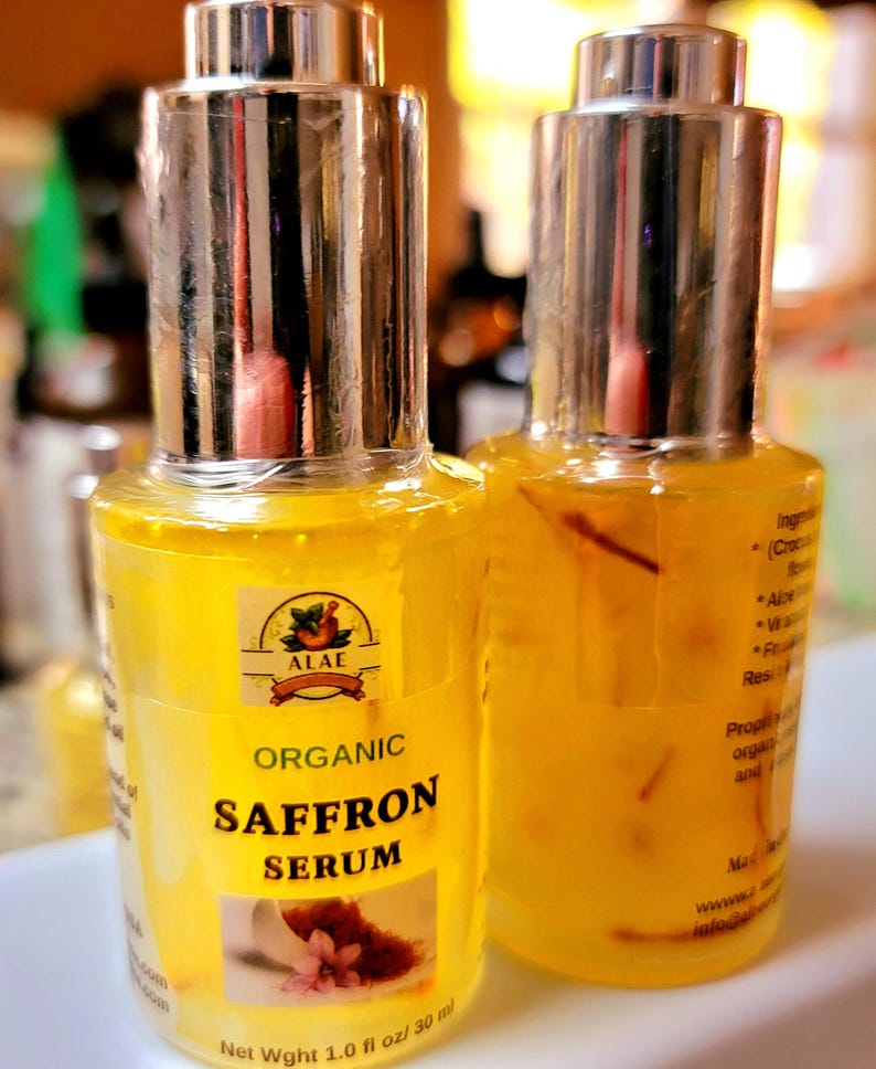 May include: Two bottles of organic saffron serum with silver caps. The yellow liquid contains saffron threads. The label reads "Organic Saffron Serum" and "Net Wght 1.0 fl oz / 30 ml".